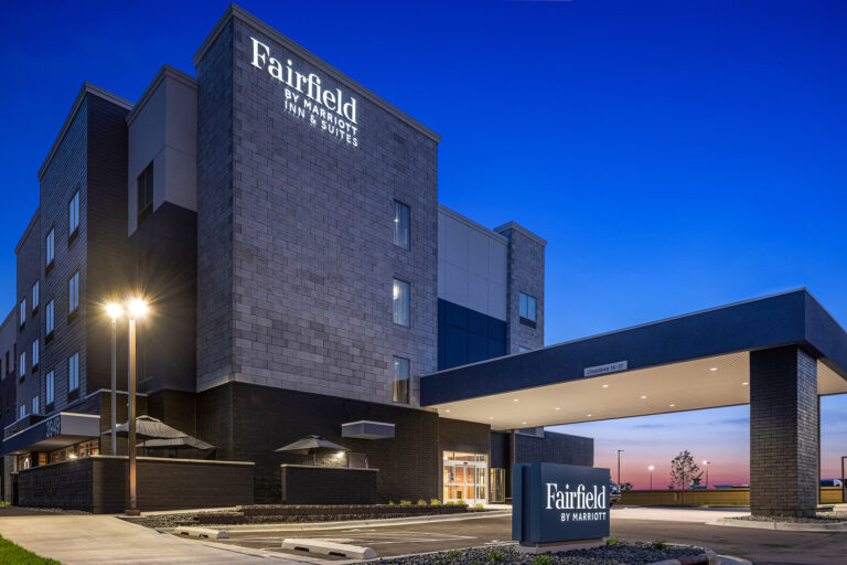 Exterior view of a Marriott Fairfield Inn at dusk, showcasing modern architecture with illuminated signs and a prominent entrance. The deep blue sky serves as the perfect backdrop for striking hotel photography, highlighting the hotel's impressive structure.
