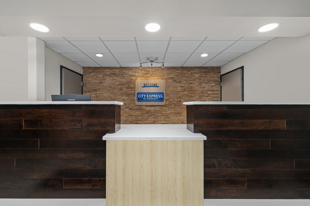 Front desk area of a hotel with a modern design, featuring a wood-paneled reception counter, Lenovo computer, and a Welcome City Express sign on a stone accent wall—perfect for guests seeking Marriott comfort in Florida.