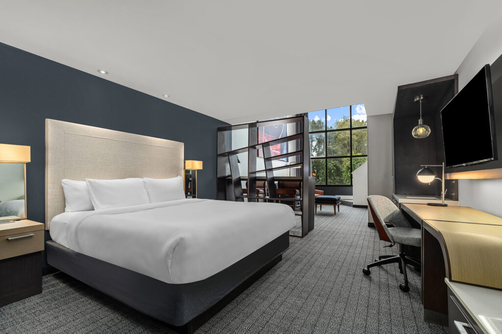 Modern hotel room in Oxford, MS with a large bed, desk, flat-screen TV, and seating area by a window. Dark accent walls and soft lighting highlight contemporary furnishings—perfect for marriott hotel photography or a comfortable stay.