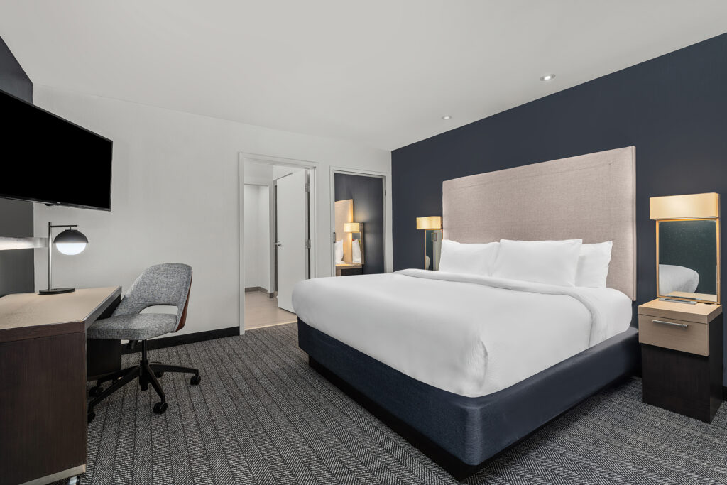 Modern Marriott hotel room with a large bed, two bedside tables with lamps, a desk and office chair, and a mounted flat-screen TV. Neutral colors and minimalist decor make it perfect for hospitality photography.